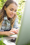 Young student lying on the grass using her laptop