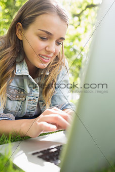 Young student lying on the grass using her laptop