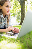 Young thinking student lying on the grass using her laptop