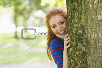 Smiling redhead hiding behind a tree