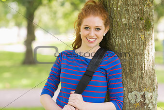 Smiling pretty redhead leaning against a tree