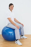 Smiling man sitting on exercise ball in hospital gym