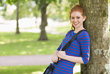 Cute redhead student leaning against a tree