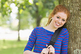 Cheerful redhead student leaning against a tree