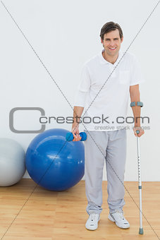 Portrait of a smiling man with crutch and dumbbell