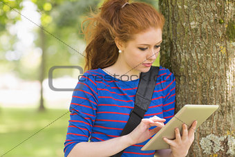 Redhead student leaning against a tree using her tablet