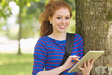 Smiling student leaning against a tree using her tablet