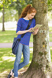 Happy student leaning against a tree using her tablet pc