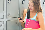 Laughing student sending a text beside lockers
