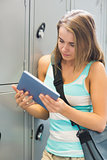 Happy student using her tablet beside lockers
