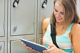 Cheerful student using her tablet beside lockers