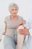Displeased senior woman getting her knee examined