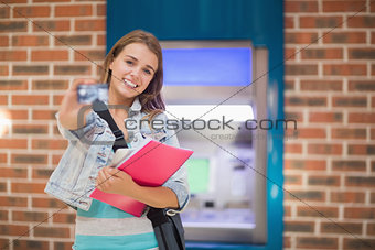 Pretty student standing showing her card to camera at the atm