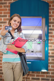 Happy student standing showing her card to camera at the atm