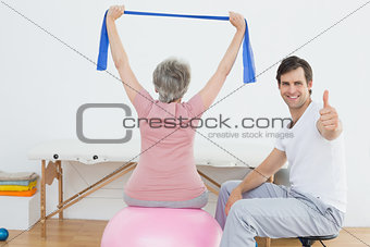 Therapist gesturing thumbs up by woman on yoga ball