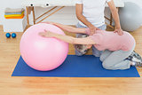 Physical therapist assisting senior woman with yoga ball