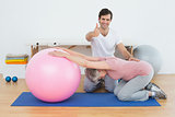 Therapist gesturing thumbs up by senior woman with yoga ball
