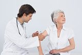 Male doctor injecting a senior female patient's arm