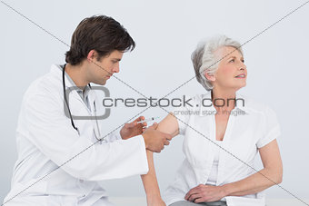 Male doctor injecting a senior female patient's arm