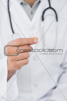 Mid section of a male doctor holding acupuncture needles