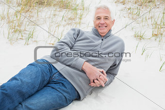 Smiling senior man relaxing on sand at beach
