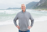 Happy senior man with hands on hips at beach