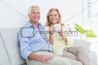 Senior couple with coffee cup sitting on sofa