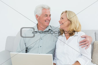 Senior couple with laptop on sofa in a house