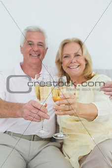 Senior couple holding out champagne flutes at home