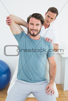 Male physiotherapist stretching a smiling man's arm