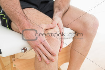 Mid section of a man with his hands on a painful knee