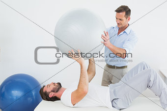 Physical therapist assisting man with yoga ball