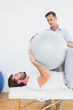 Physical therapist assisting young man with yoga ball
