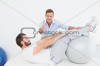 Therapist gestures thumbs up while assisting man do sit ups