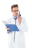 Serious doctor with clipboard talking on wireless radio