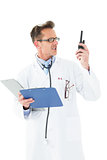 Annoyed doctor with clipboard talking on wireless radio