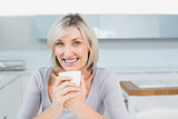 Smiling young woman with coffee cup in kitchen at home