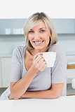 Smiling casual young woman with coffee cup in kitchen