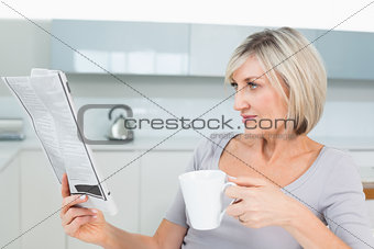 Woman drinking coffee while reading newspaper in kitchen