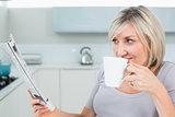 Woman drinking coffee while reading newspaper