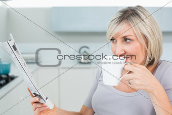 Woman drinking coffee while reading newspaper