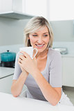 Thoughtful smiling woman with coffee cup in kitchen