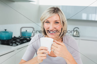 Smiling casual woman with coffee cup in kitchen
