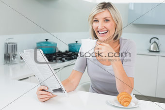 Happy woman with coffee cup and newspaper in kitchen