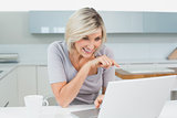 Casual woman with coffee using laptop in kitchen