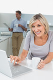 Woman using laptop and man reading newspaper in kitchen