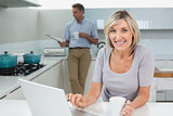 Woman using laptop and man reading newspaper in kitchen
