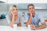 Bored couple sitting with coffee cups in kitchen