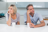 Displeased couple sitting with coffee cups in kitchen