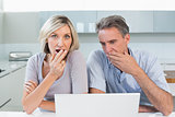 Shocked couple with laptop in kitchen